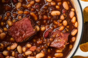 A pot of homemade baked beans with tomato sauce, bacon, and spices, served in a rustic setting.