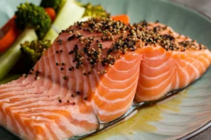 Raw salmon slices on a plate with lemon slices.